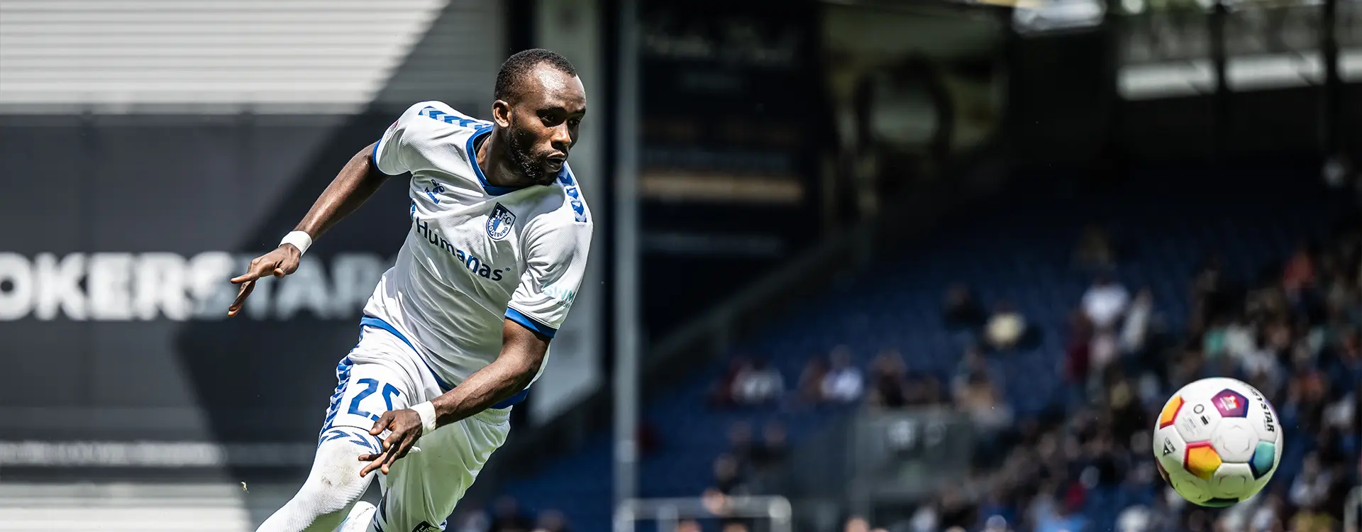 This is a split image showing different scenes and players from a football match. The upper portion of the photo is an action shot of a player in mid-play, looking up with intense focus, as if just scored or about to. Below that, on the left side, is a black and white shot of two blurred figures on a field, likely playing a sport, with one player in action and another standing still. The right side of the image displays a person seated, wearing a light blue jersey with dark shorts and cleats, who looks to be watching the game or waiting to join in play. All three images depict moments from what appears to be an indoor football pitch due to the artificial turf and bright lighting.