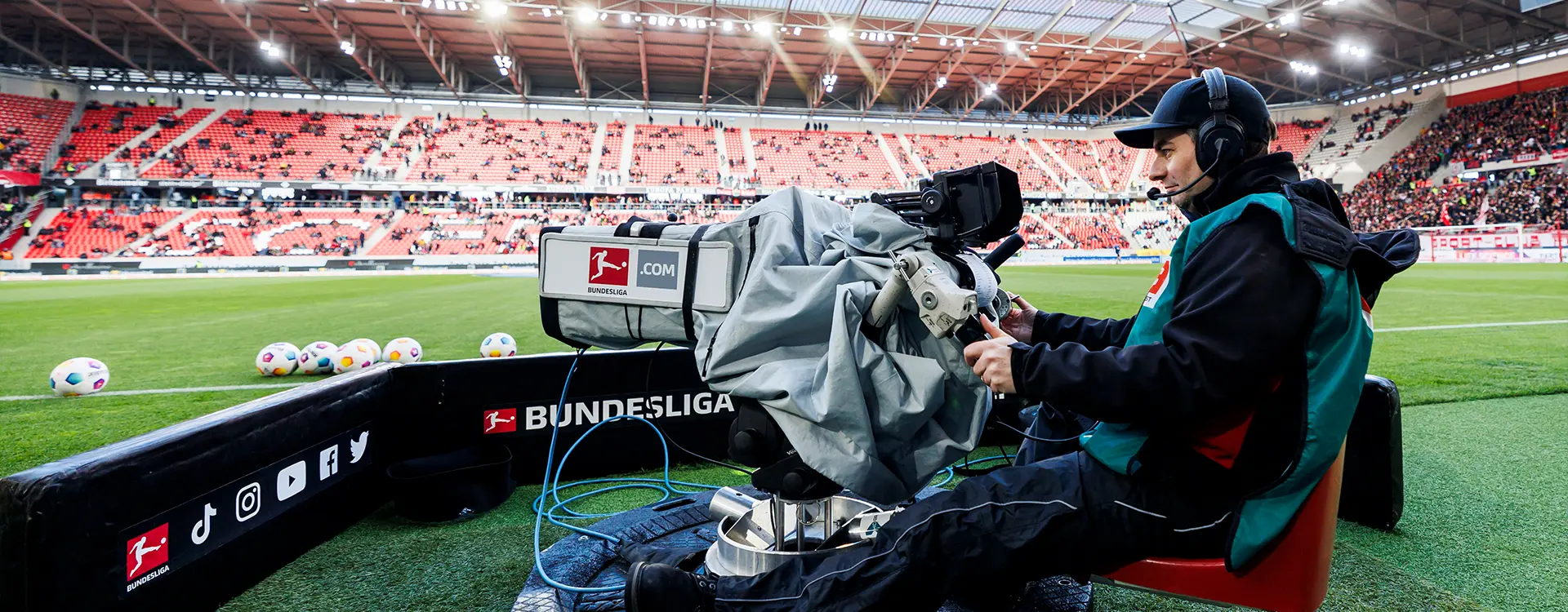 It seems like you've shared an image of a live television broadcast at a European football match. The image features a man sitting in front of a television camera, presumably a commentator or presenter who is providing commentary on the game to the audience watching at home on TV. Behind him is a sports commentary desk equipped with audio and video equipment for recording and broadcasting his commentary.
On the field, you can see players engaged in the sport of football. Some areas of the spectator stands are clearly visible, suggesting that there are more people present than what we see through the stadium lens.
The image has been somewhat distorted, as it appears to be a screenshot taken from a video that was paused and then resumed while the video player software was overlapping on the bottom of the image. This creates an overlay effect on the bottom left corner of the photo, and part of the right side appears darker than usual possibly due to the transparency of the layer.
The watermark "Spectrum Photography" overlays the image, indicating that this photograph may be taken by a photography company specializing in sports, event location, or media content capture.