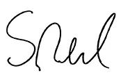 In the image, there is a signature that appears to be by Shahrukh Khan, as indicated by the handwritten text next to the signature. The background suggests it might have been taken on paper. The quality of the image is not very high. There is no other significant detail visible in the photograph.