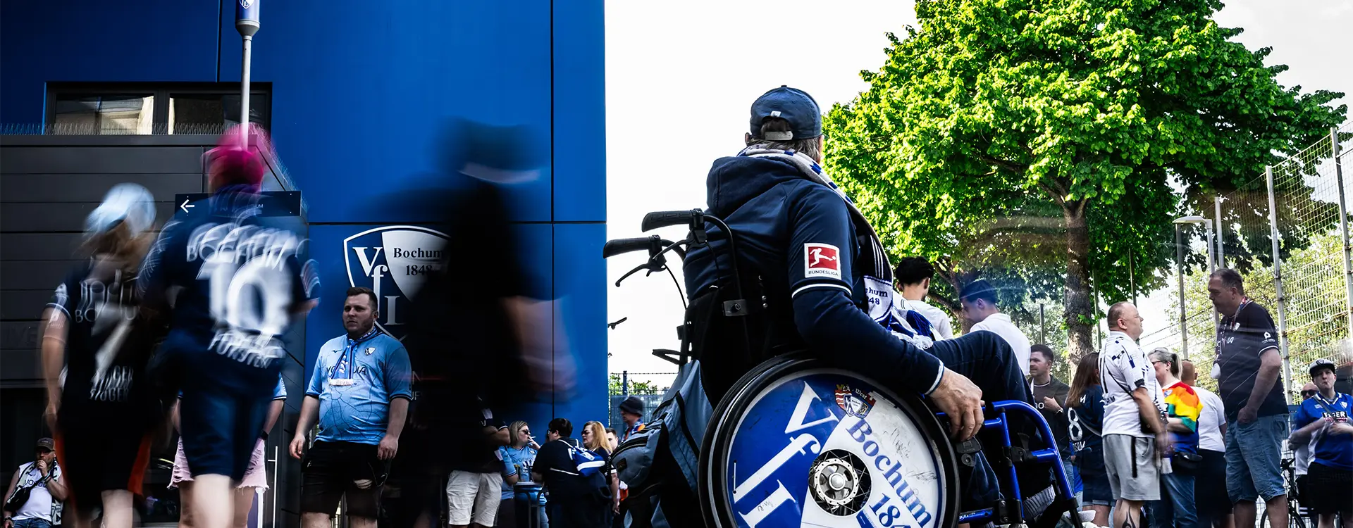 The image is a collage that shows two different scenes. On the left, there's an action shot of someone playing an instrument. On the right, it depicts a crowd of people, possibly attending a sports event or some other gathering, given the presence of individuals with logos and a person on a wheelchair, which could indicate an accessibility area at the event. Both images appear to be taken from a distance and may not have a clear focus due to the angle and compression required for stitching them together.