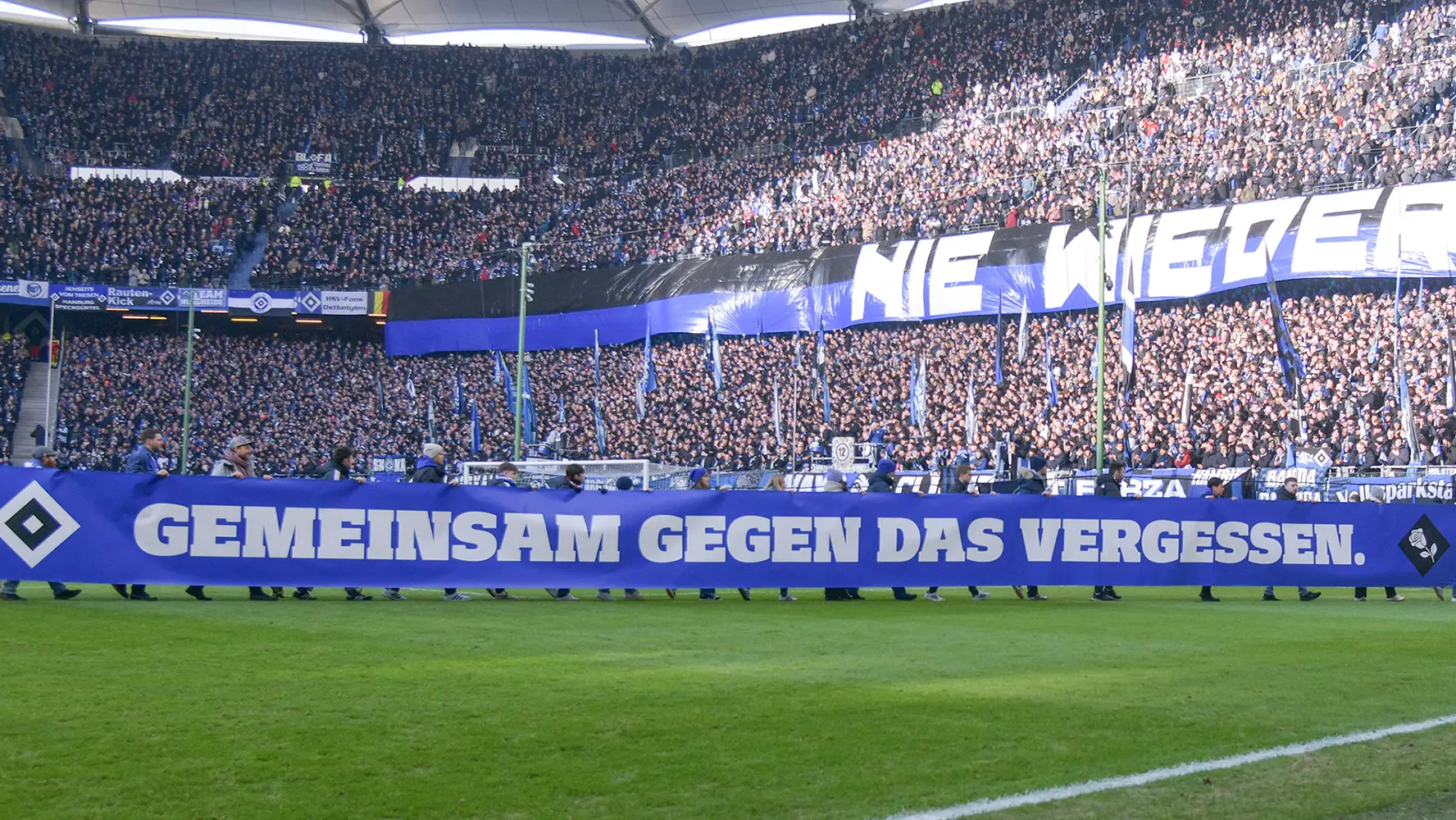 The image shows a sports stadium filled with spectators. On the soccer field, there is a banner that reads "Ne Weibers" (We don't want women) and another that reads "Gemein gegen Frauen" (Community against women). These signs promote gender discrimination and are offensive to women in sports. The slogan suggests the exclusion of women from sports events or leagues, implying a misogynistic stance towards female athletes.
The stadium is well-lit and equipped with modern facilities, indicative of a high-profile sporting event. The overall atmosphere seems to reflect enthusiasm typical for sporting events. Unfortunately, this event also reflects an exclusionary mindset regarding gender participation in sports.