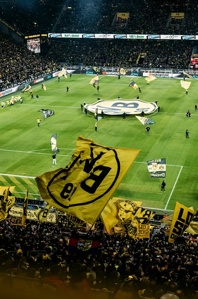 Der Einzug des BVB Teams in ein Fußballstadion. Fans schwenken BVB Fahnen auf den Tribünen. (Foto)
