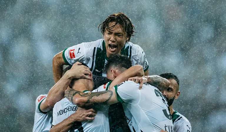 Ko Itakura of Borussia Mönchengladbach leans on his jubilant teammates. (Photo)