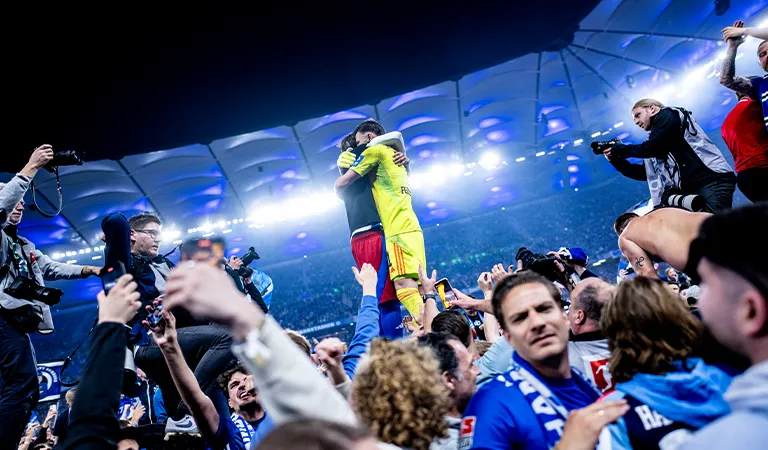 The HSV goalkeeper and another player embrace on the pitch after promotion. (Photo)