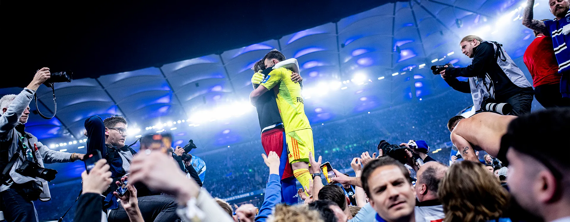 The HSV goalkeeper and another player embrace on the pitch after promotion. (Photo)
