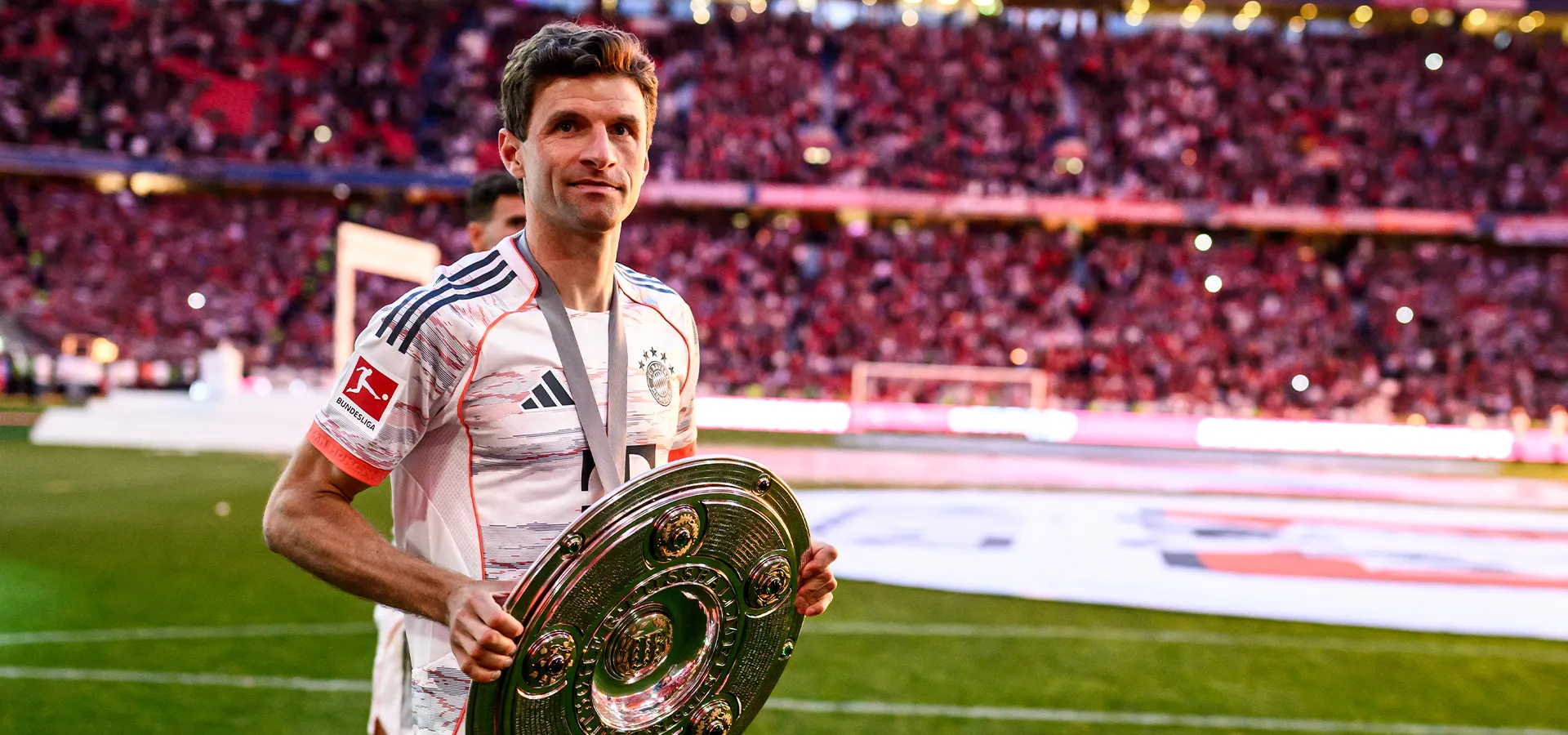 Thomas Müller holds the Bundesliga championship trophy in his hands and smiles at the camera. (Photo)